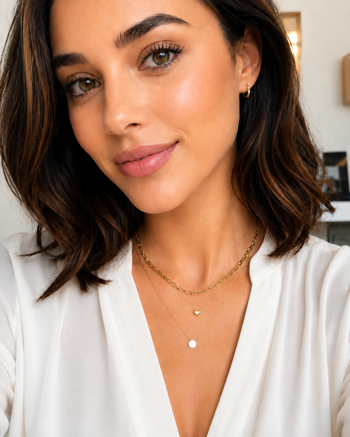 Model wearing the Claire gold heart necklace layered with two delicate gold necklaces and a white blouse