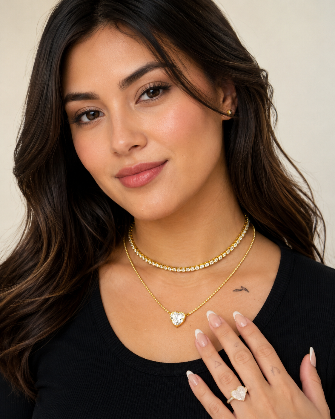 Model wearing the Clara gold tennis choker layered with a delicate heart pendant necklace.