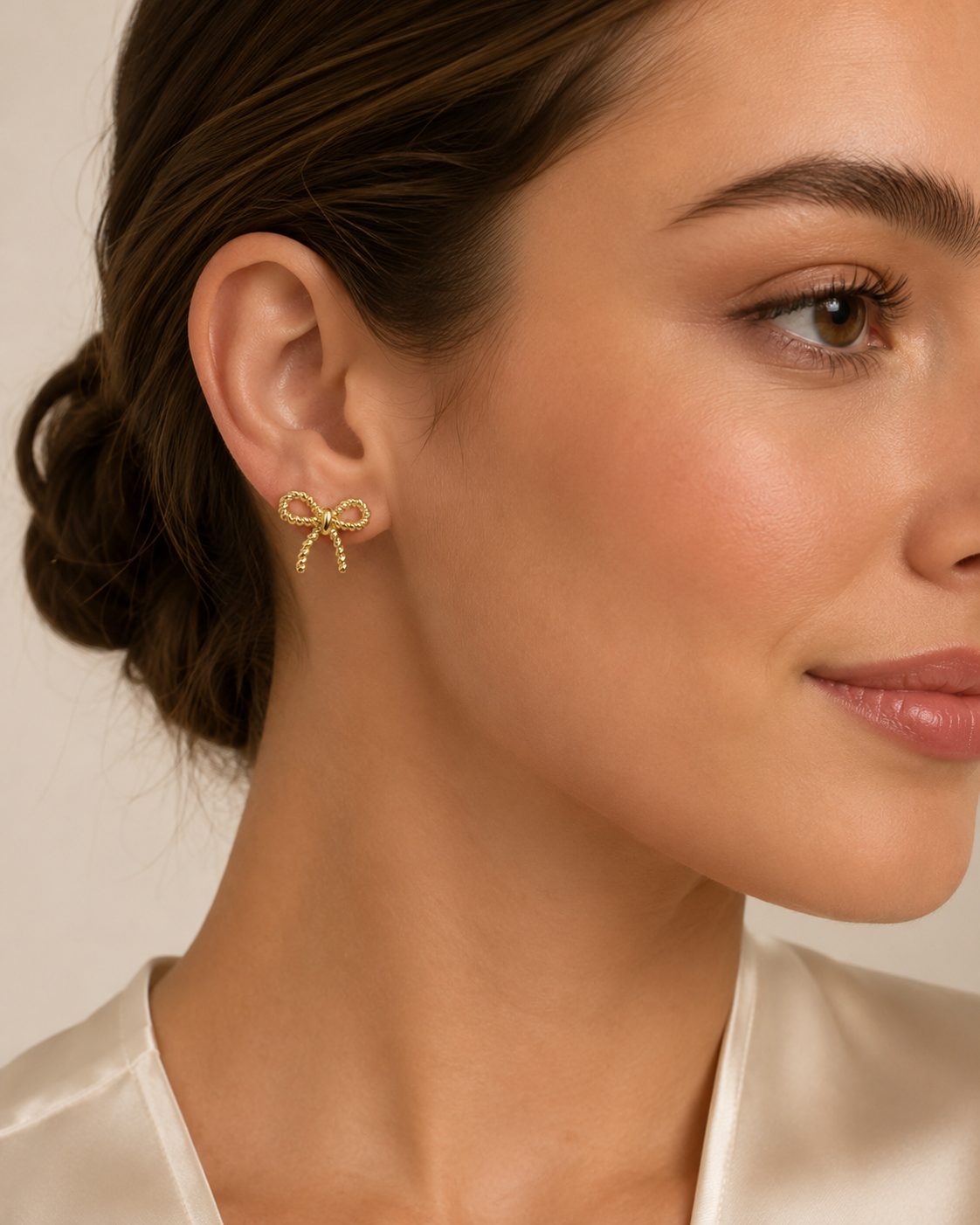 Model wearing the Colette gold bow stud earrings against a soft neutral background.