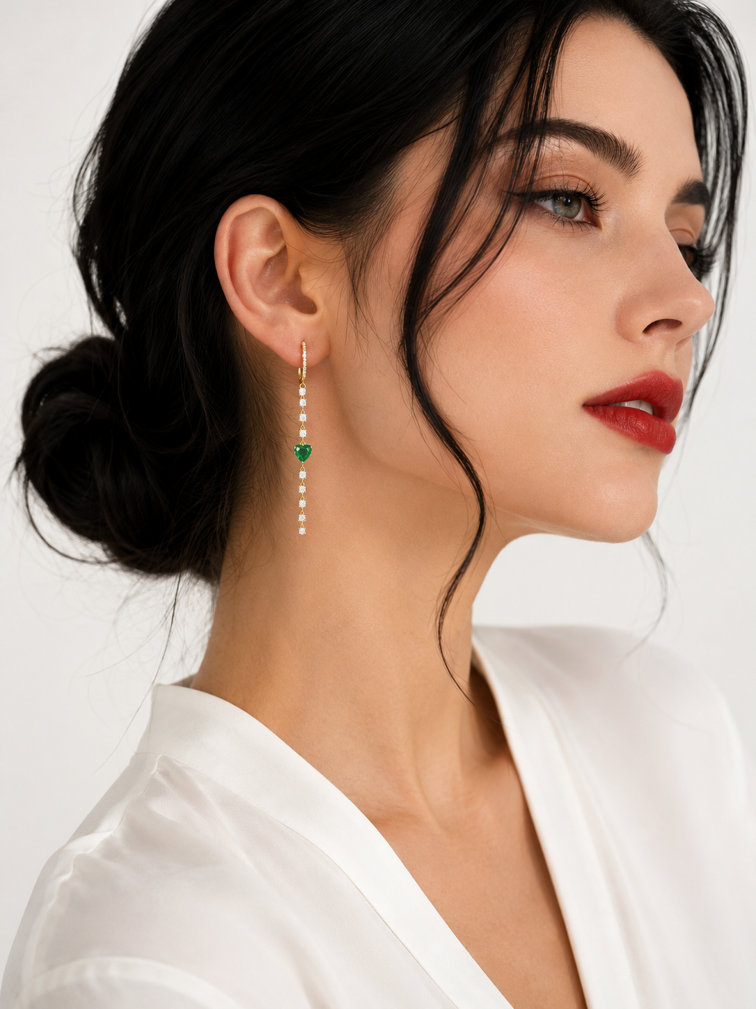 Model wearing Monica 14k gold-plated sterling silver drop earrings with green heart-shaped emeralds and clear simulated diamonds
