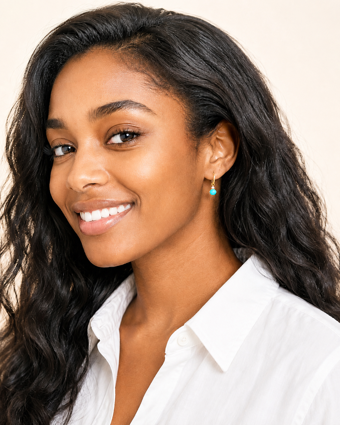 Smiling model wearing gold hoop earrings with turquoise stone drops